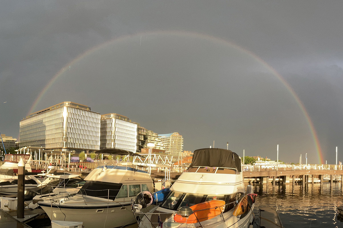Color Photo Showing Golden Evening Light and Full Arc Rainbow over Boats.